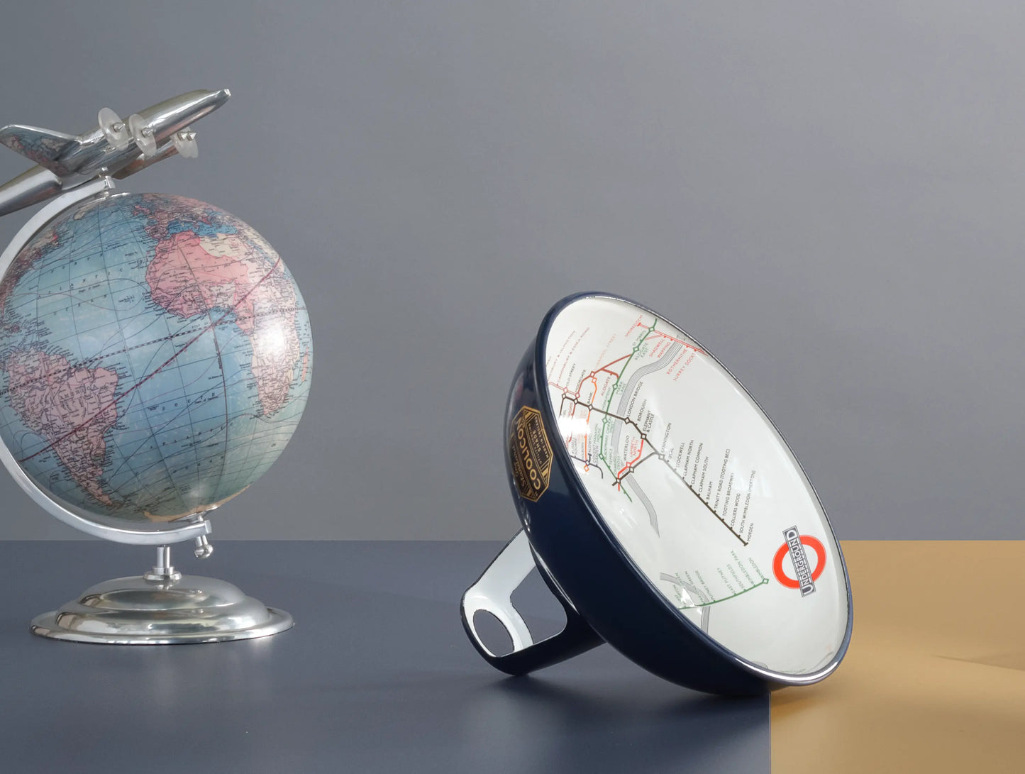 An Original Piccadilly Line Blue shade on a table. On its left is a globe with a metal plane attached to the top.