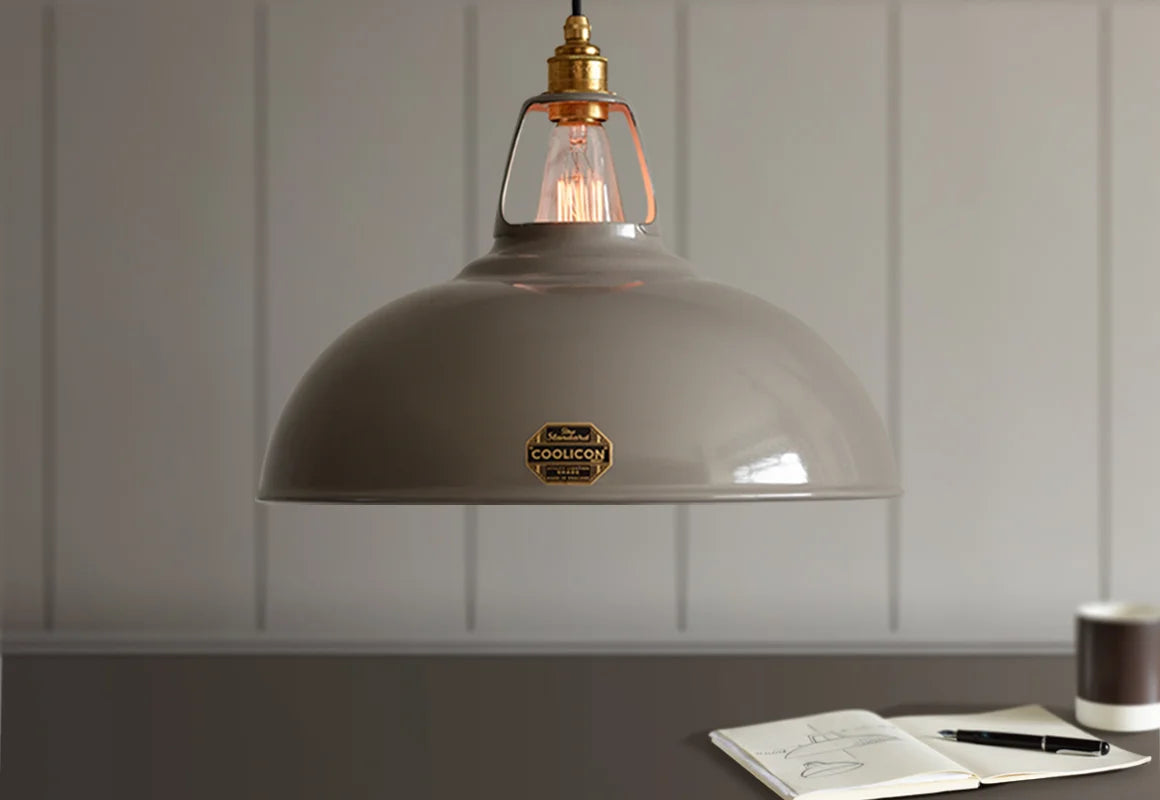 A Large Coolicon Original Grey lampshade hanging over a table. Below is an open sketchbook and a grey coffee cup.