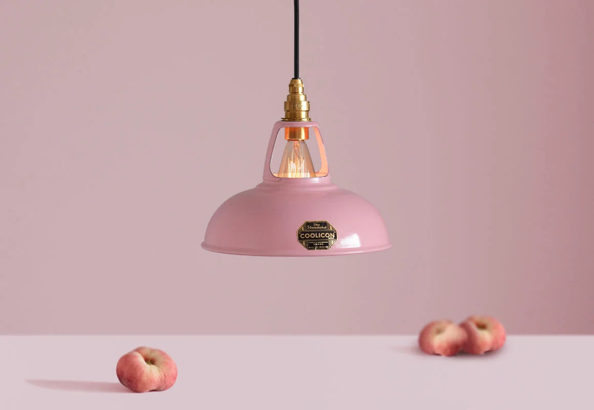 A Coolicon Powder Pink lampshade with a Brass pendant set hanging above a plinth with a bowl of flat peaches.