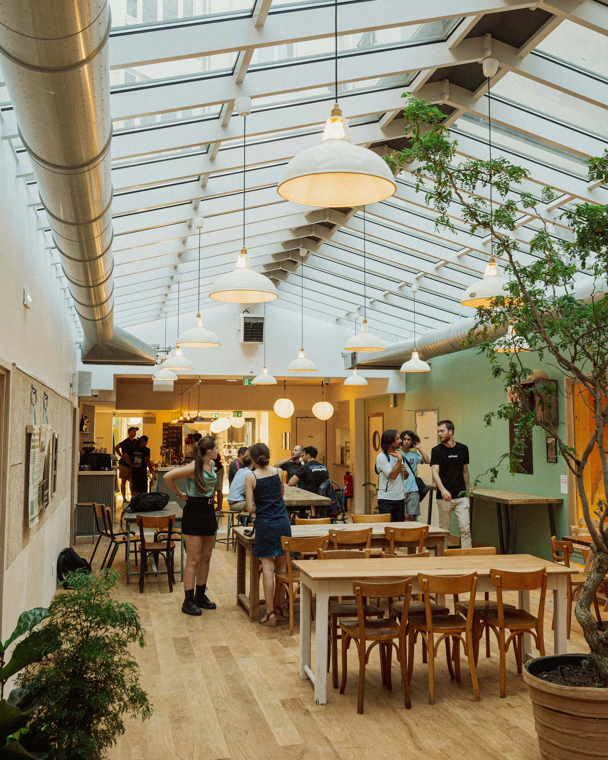 Cluster of Coolicon heritage pendant lights above communal seating in Arkose’s bouldering gym, softening the industrial architecture with warm bi‑directional light.