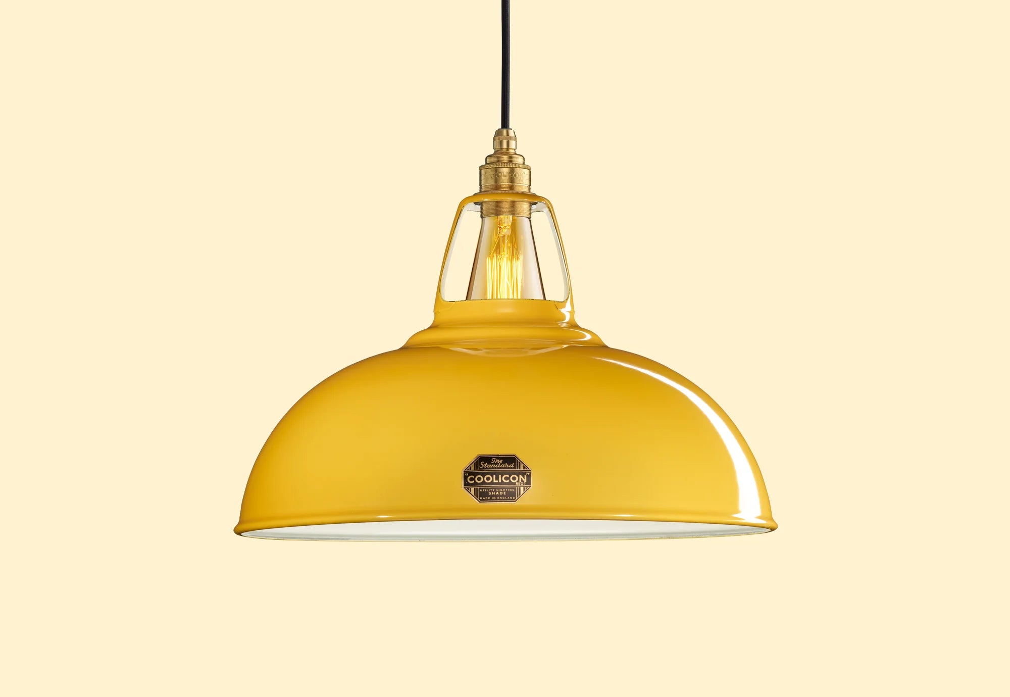 A Large Yellow Enamel pendant lampshade hanging in front of a neutral yellow background.