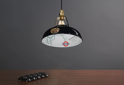 An Original Northern Line Black shade hanging over a wooden table with a line of toy cars of black taxis.