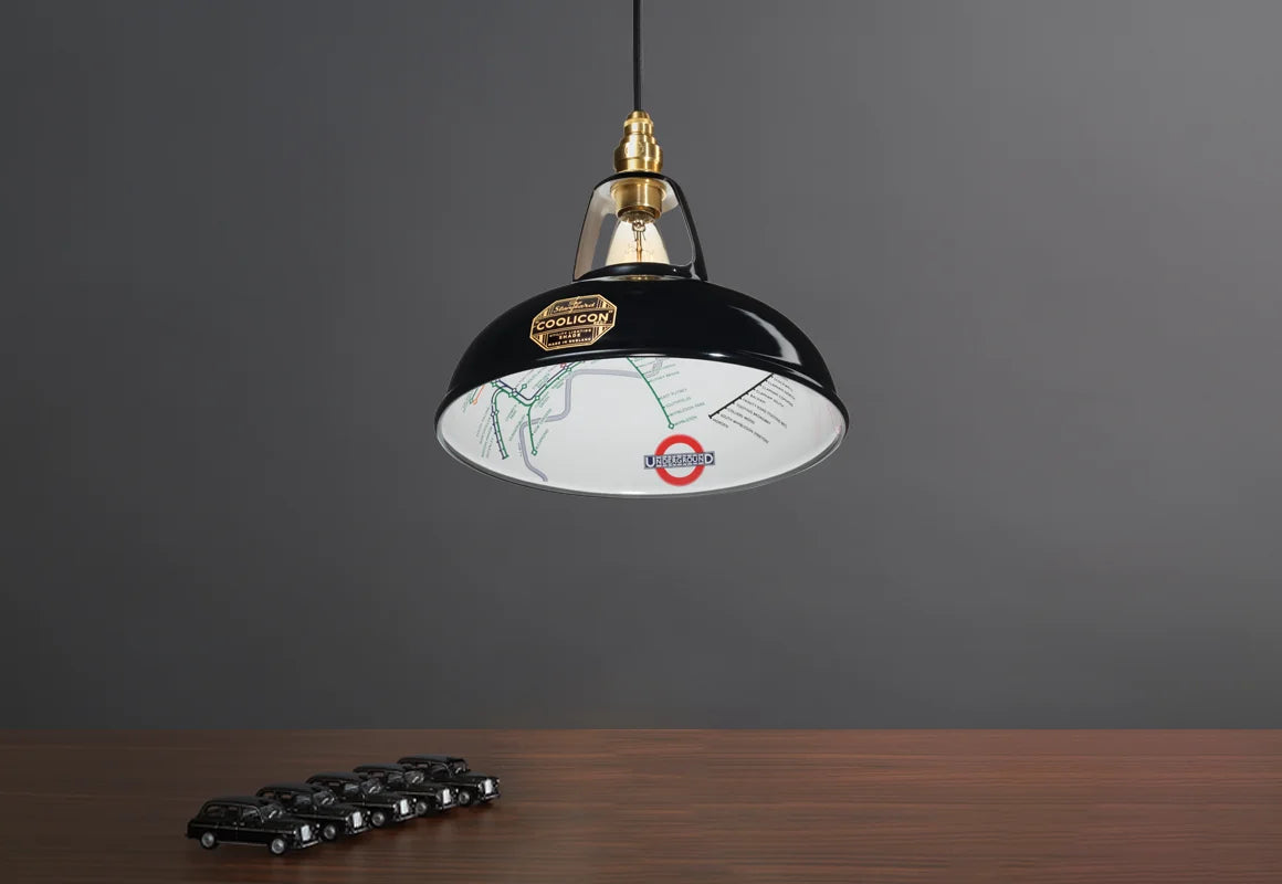 An Original Northern Line Black shade hanging over a wooden table with a line of toy cars of black taxis.