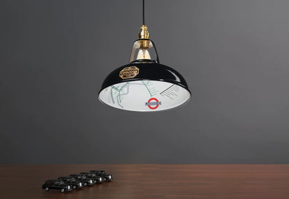 An Original Northern Line Black shade hanging over a wooden table with a line of toy cars of black taxis.