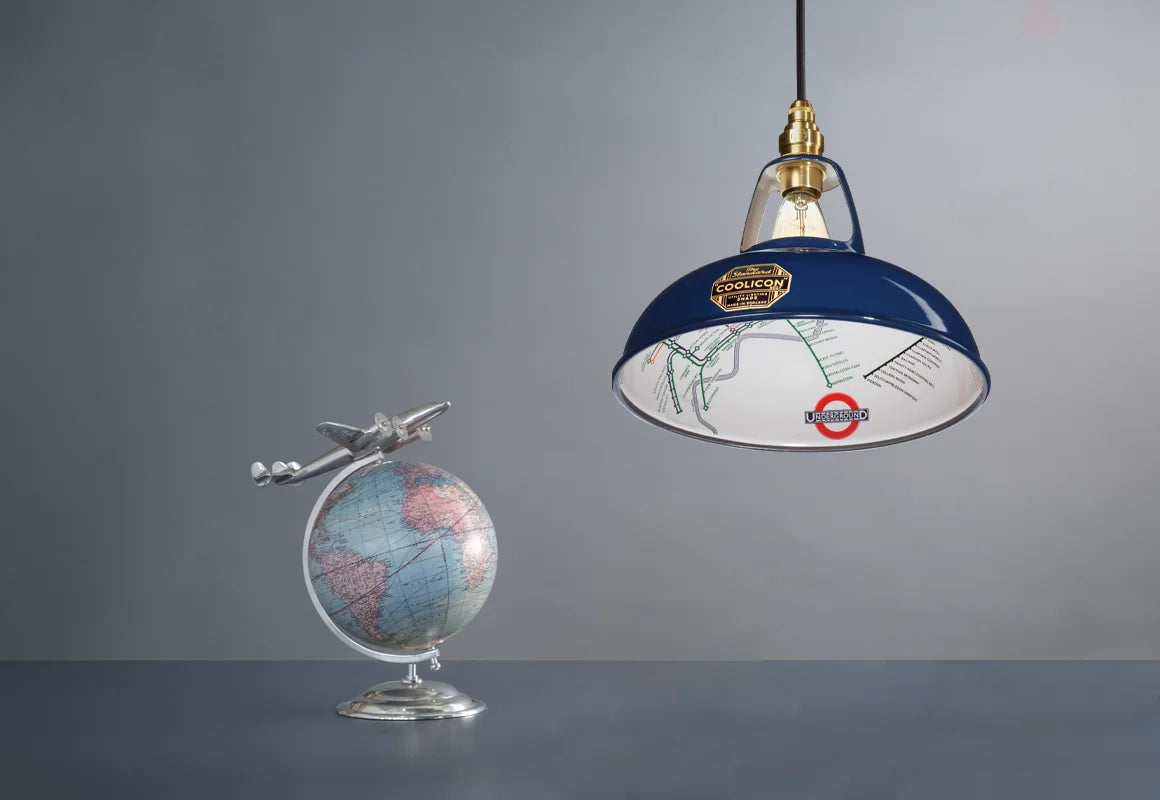 An Original Piccadilly Line Blue shade over a table. On its left is a globe with a metal plane attached to the top. 