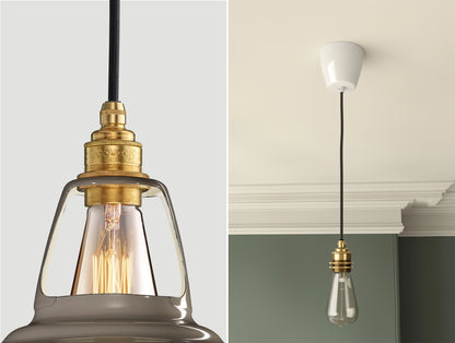 Close up of an E27 Signature Brass suspension set on an Original Grey lampshade on the left. On the right, an E27 Brass pendant set with a lightbulb is hanging from the ceiling