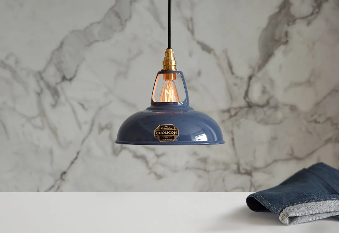 A Coolicon Selvedge blue lampshade with a Signature Brass pendant set hanging above a table with a pair of jeans. The background is a marble wallpaper.