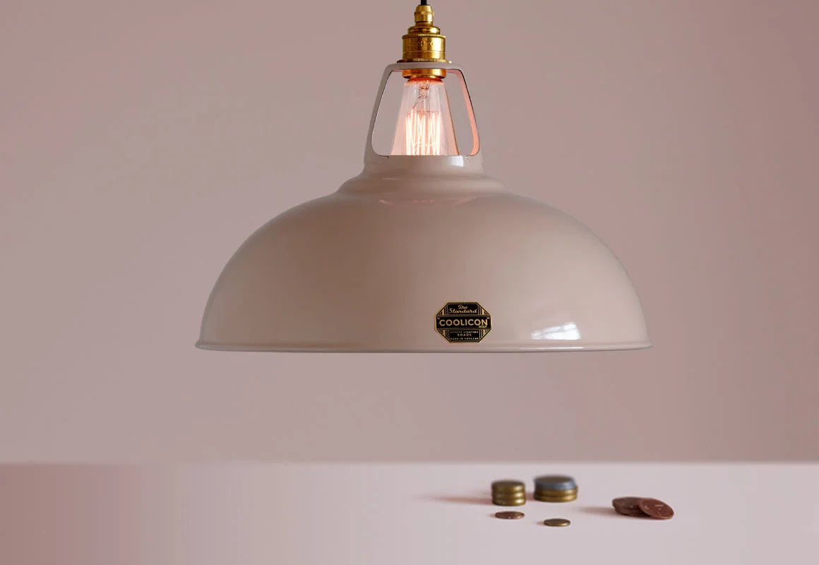 A Large Coolicon Latte Brown lampshade with a Brass pendant set hanging above a table with coins