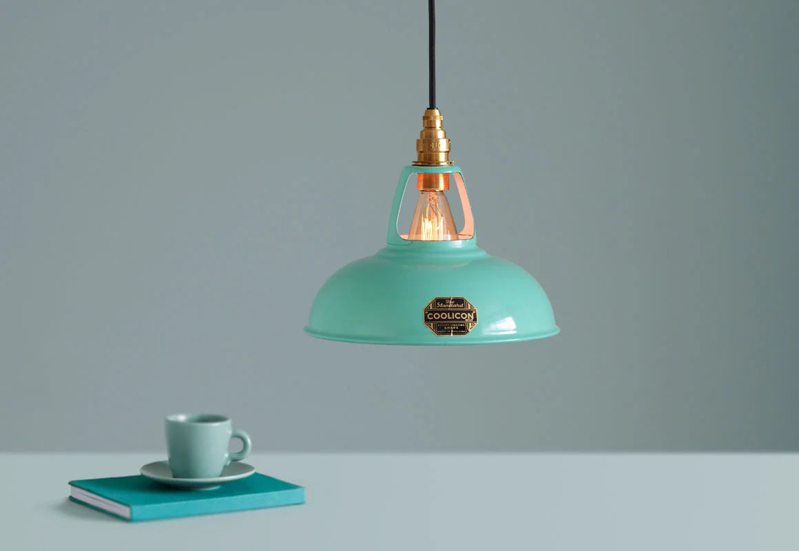 A Coolicon Fresh Teal lampshade hanging over a table. Below the shade is a teal espresso cup and saucer.