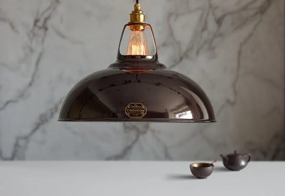 A Large Coolicon Pewter grey lampshade with a Signature Brass pendant set hanging above a table with a matching set of dark tea accessories. 