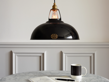 A large Jet Black shade hanging over a table above a black coffee cup, a black fountain pen and an open sketchbook. There is a sketch of a Coolicon shade on the page.