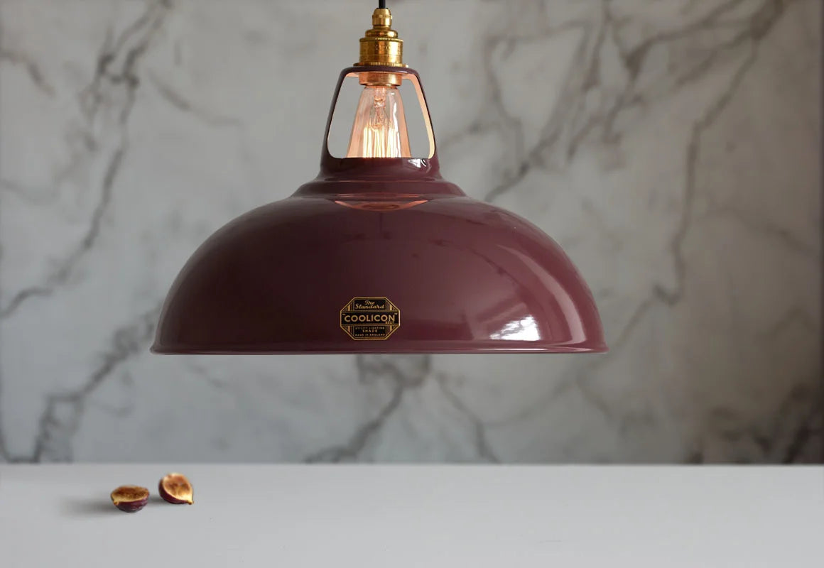 A Large Coolicon Metropolitan burgundy lampshade with a Signature Brass pendant set hanging above a table with figs.
