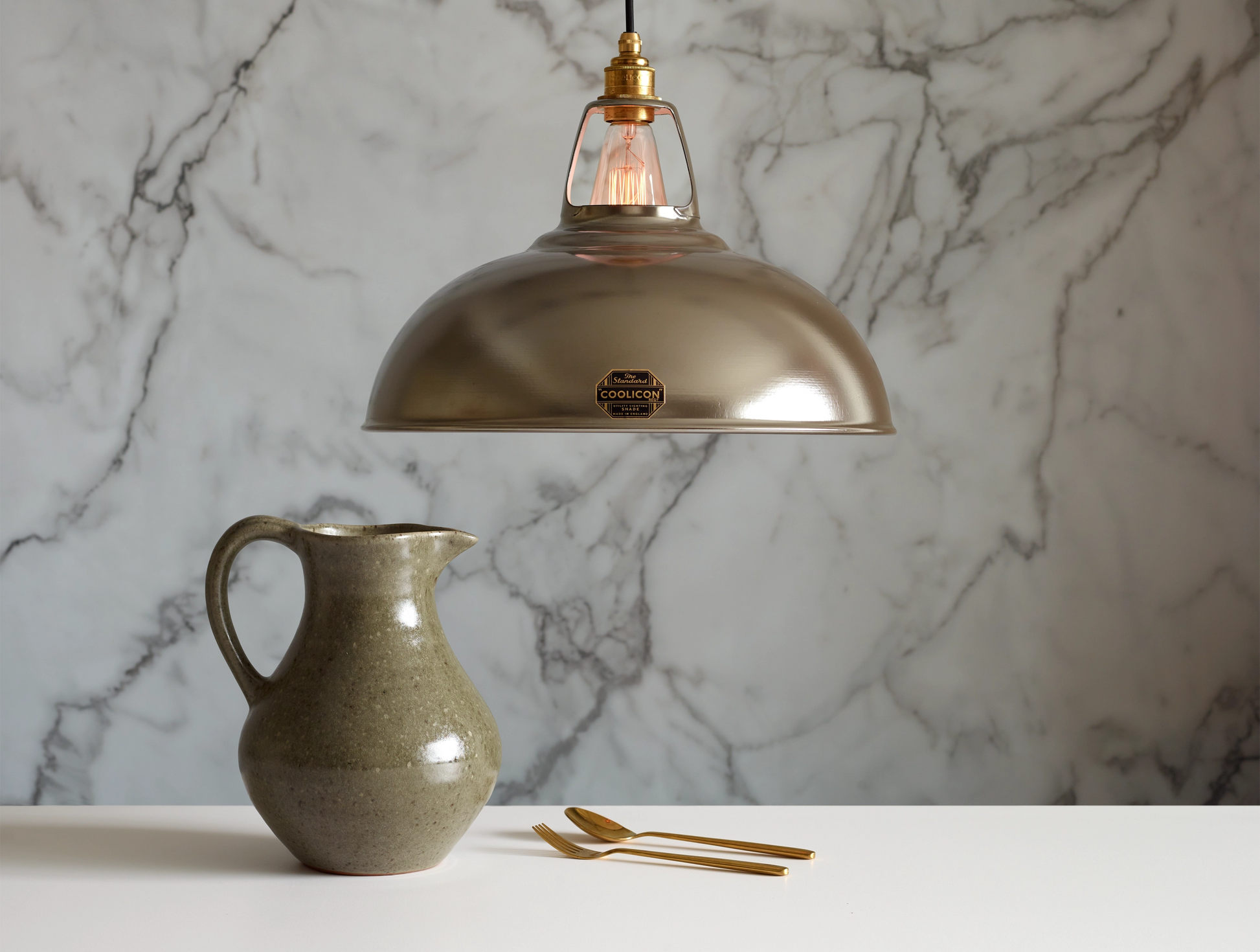 A large Antinium shade hanging over a table above a grey water jug and a golden spoon and fork. The background is a marble wallpaper