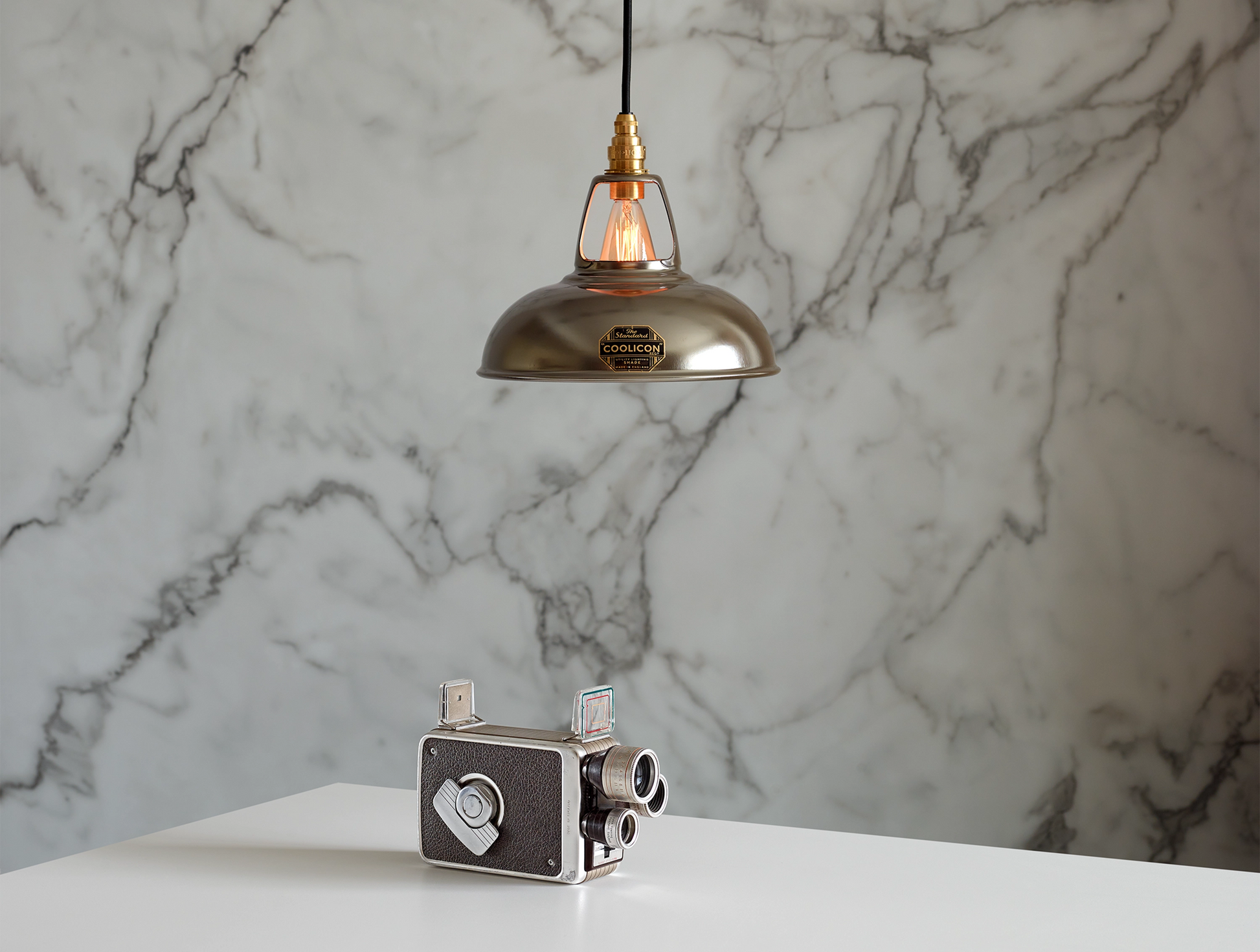 An Original Antinium shade hanging over a table above an old film camera. The background is a marble wallpaper