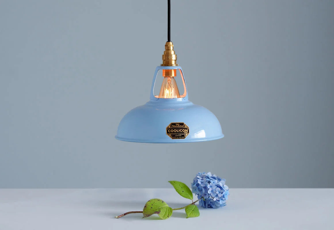 A Coolicon Sky Blue lampshade with a Brass pendant set hanging above a plinth with a blue hydrangea flower