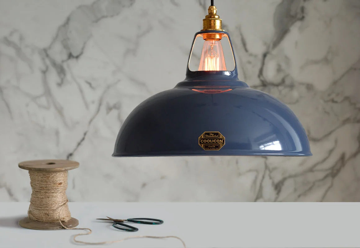 A Large Coolicon Selvedge blue lampshade with a Signature Brass pendant set hanging above a table with a spool of twine and some scissors
