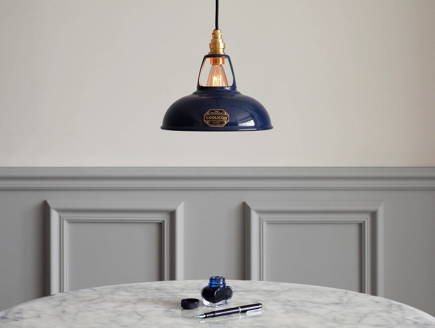 An small Royal Blue Coolicon shade hanging over a marble table. There is a bottle of blue ink and a fountain on the table
