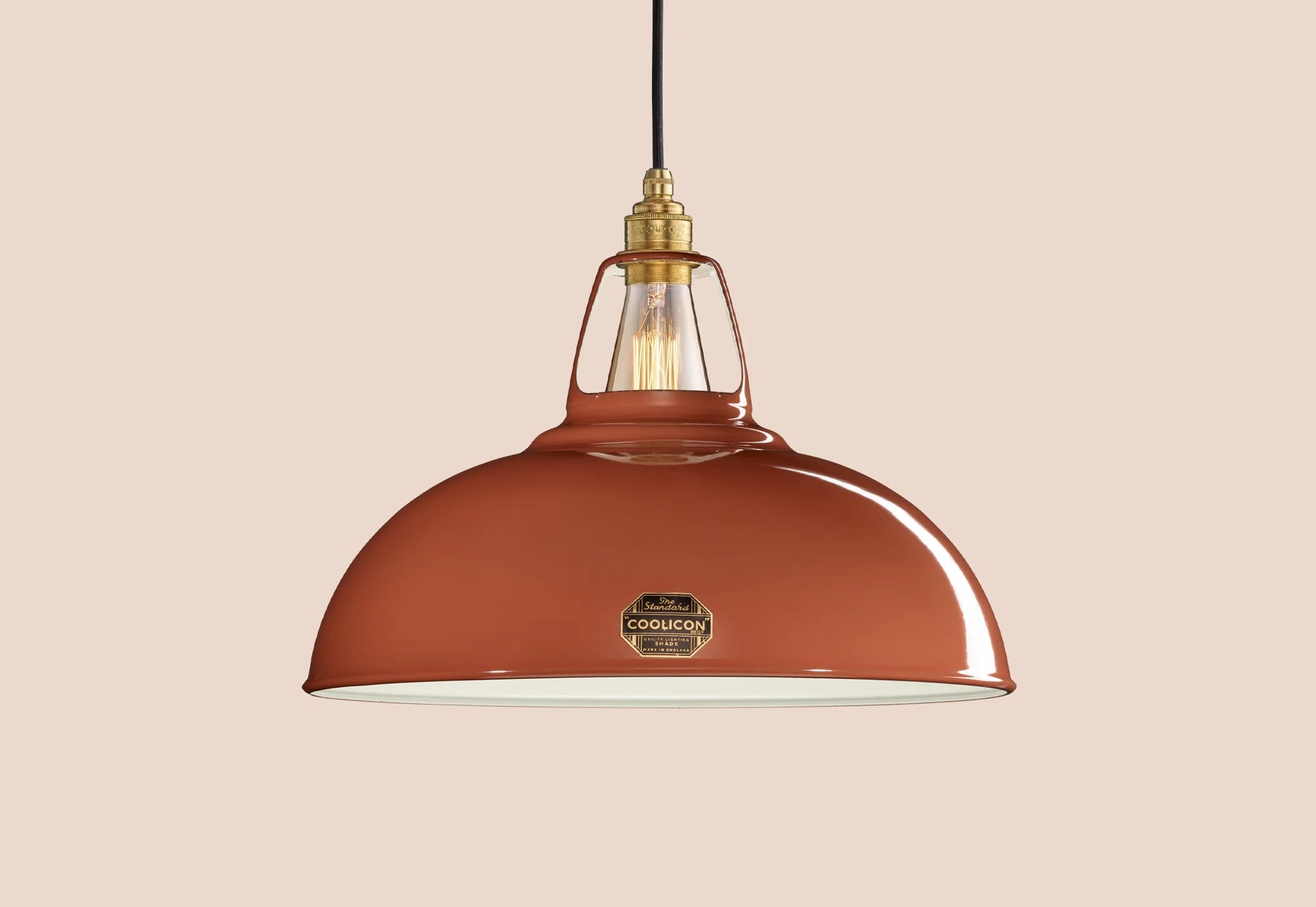 A Large Terracotta colour Enamel pendant lampshade hanging in front of a neutral orange background.