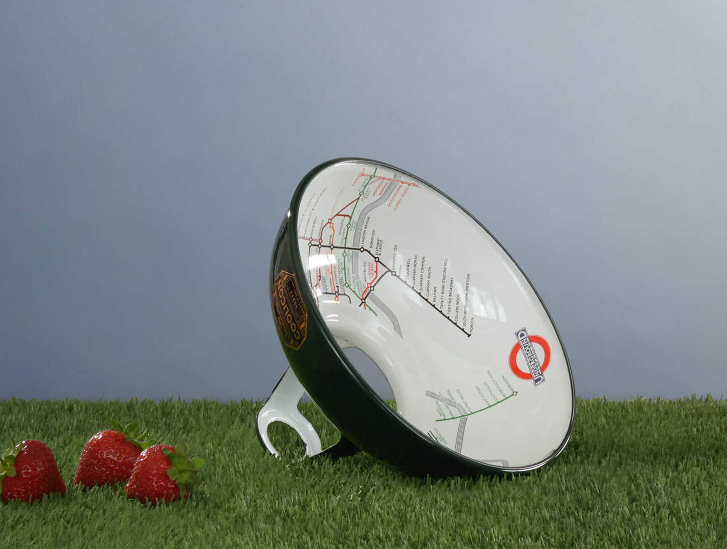 An Original District Line Green shade on a patch of grass. In the foreground are 3 red strawberries