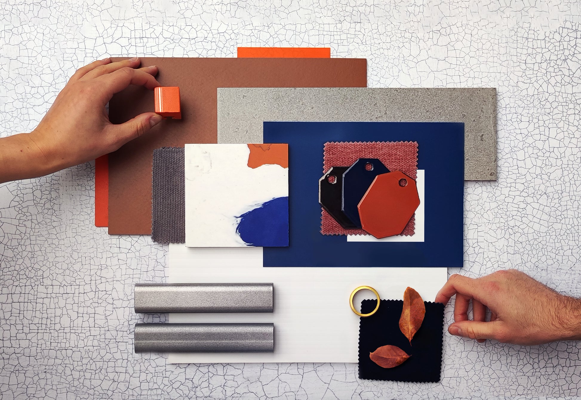 Different materials are laid out flat with one hand holding a piece of wood and one hand touching a fabric sample. Three Coolicon Vitreous Enamel swatches are in the centre