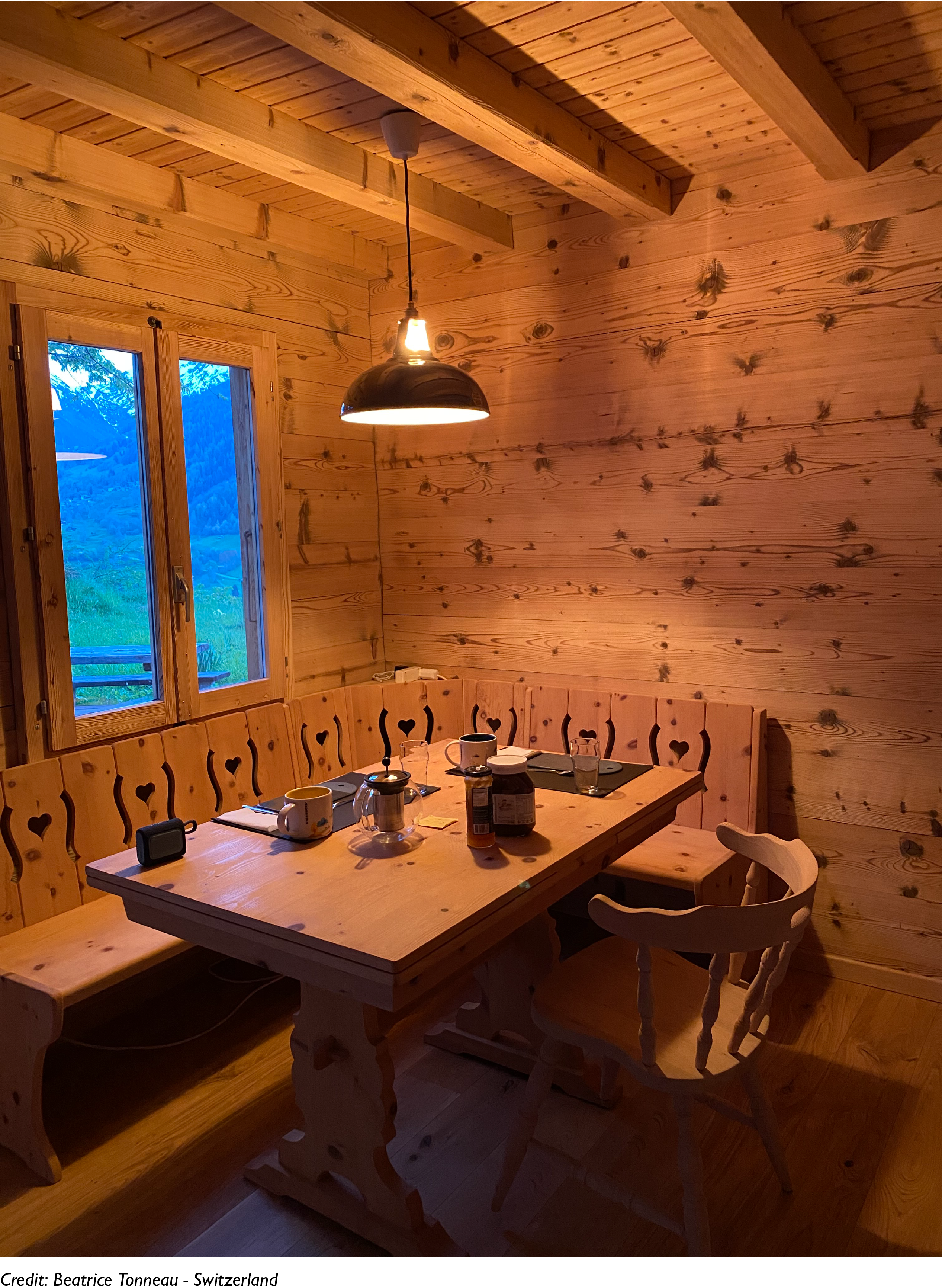 A large Pewter lamp hangs over a wooden breakfast table in a chalet