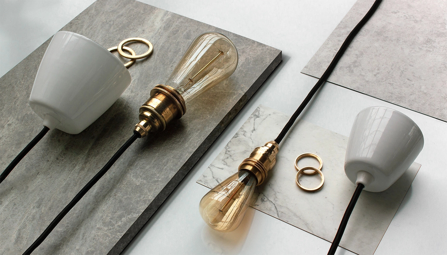 A laydown shot of a white enamel ceiling cup next to an E27 Brass lamp holder and some shade rings. On the right, an E14 brass suspension set with another white enamel ceiling cup