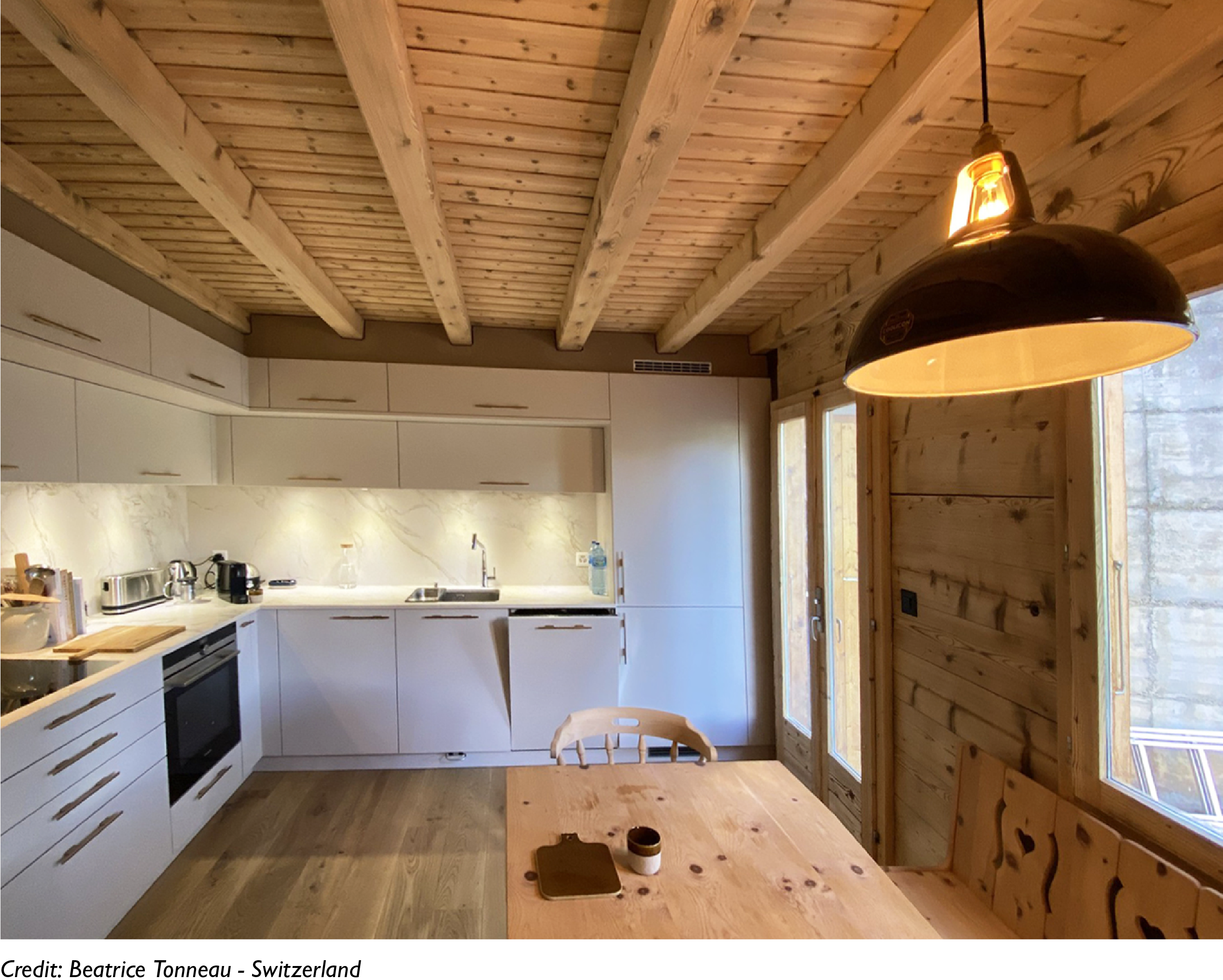 A Large Pewter lampshade hangs over a wooden table in a chalet