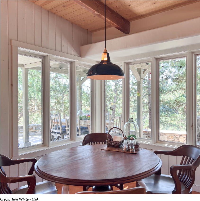 A Large Selvedge lampshade hangs over a round dining table in front of tall windows