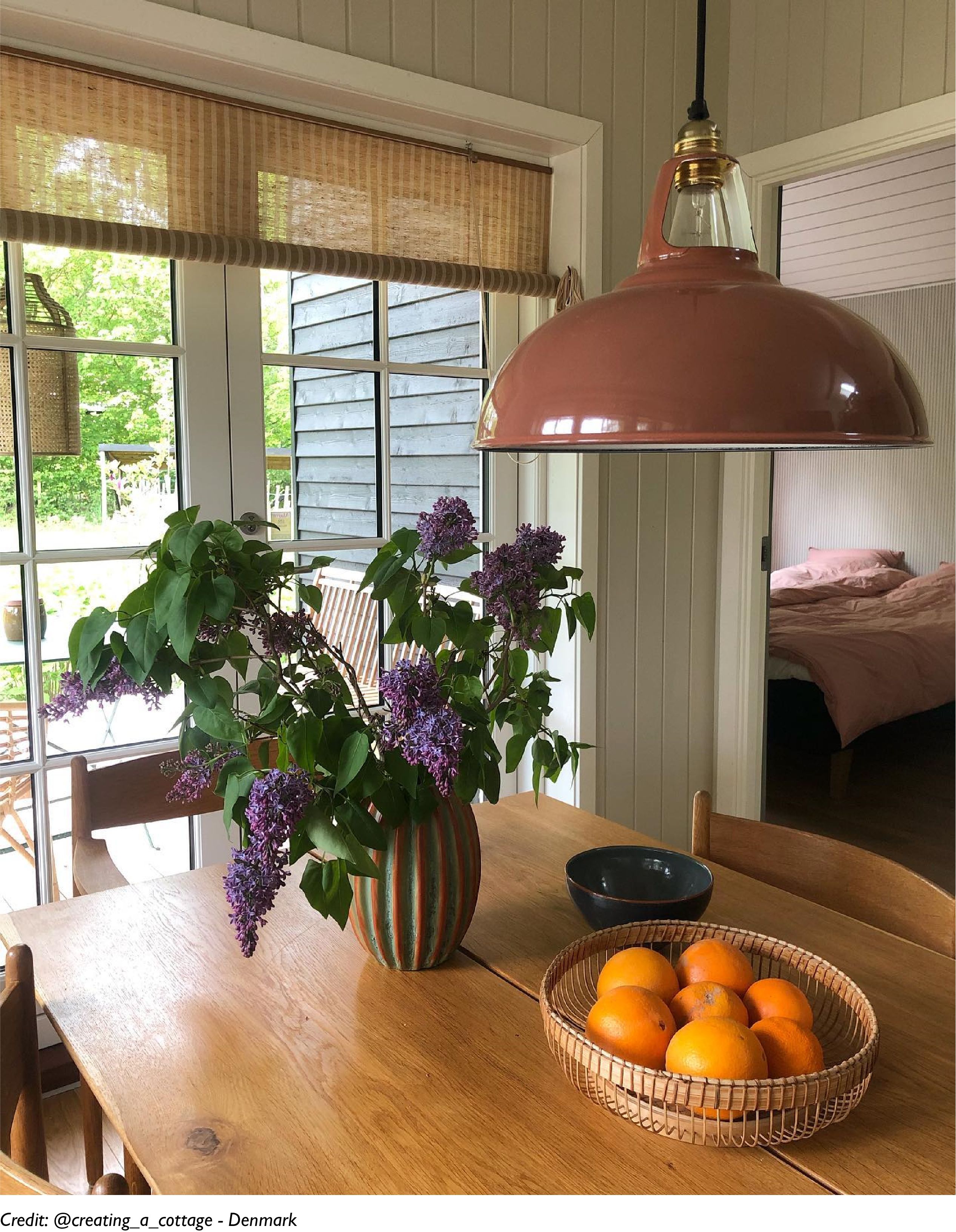 A Large Terracotta lamp shade hangs over a fruit basket on a wooden dining table
