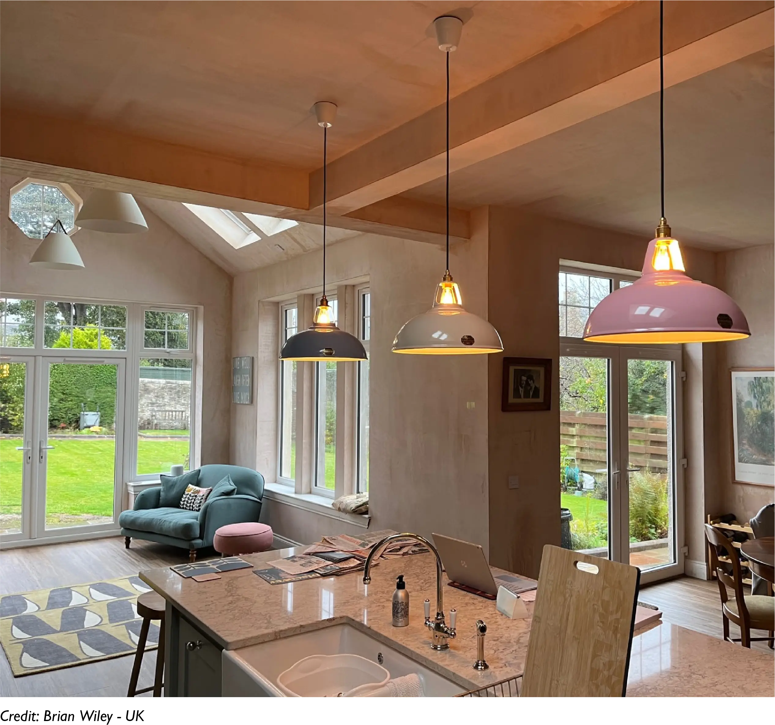 Three large lampshades hang over a kitchen island in an open plan living room with an extension