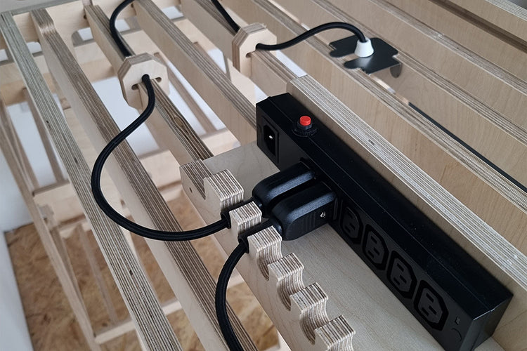 Two black electrical integrated IEC connectors plugged in to a Kettle Lead, on top of a plywood shelf.
