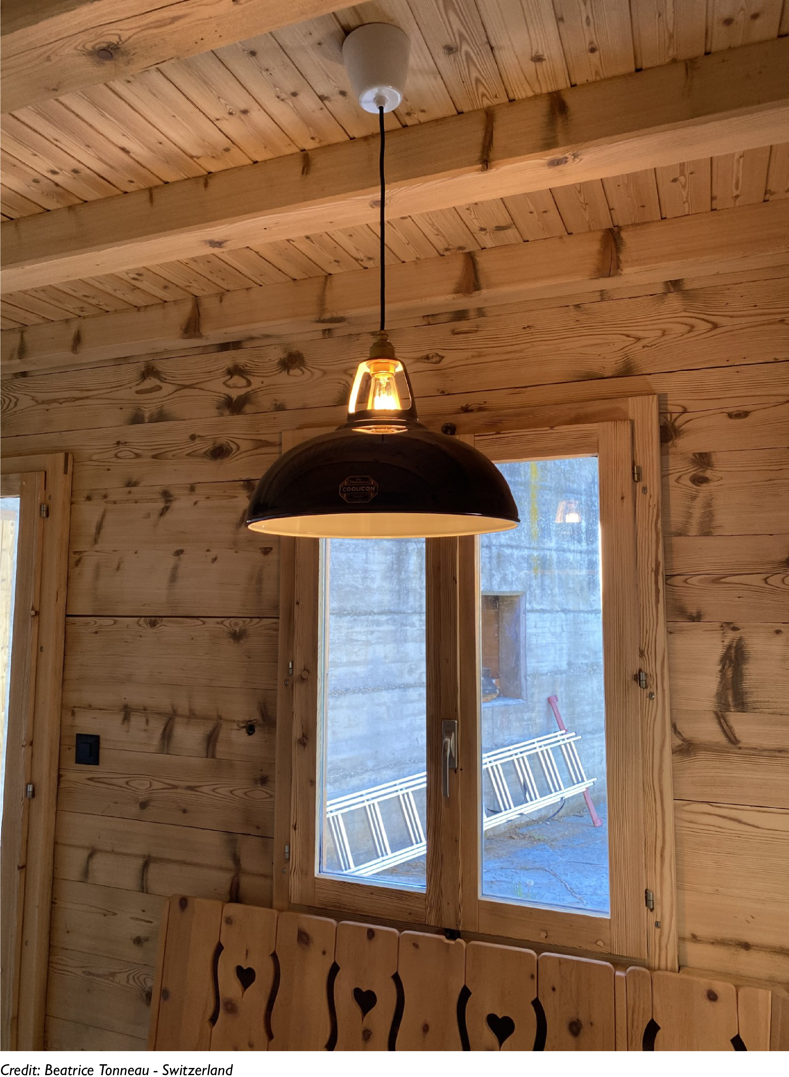 A Pewter Coolicon lampshade hangs in front of a window in a wooden interior