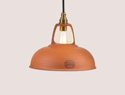 A Natural Terracotta Coolicon shade with a Signature Brass pendant set hangs over a light brown background
