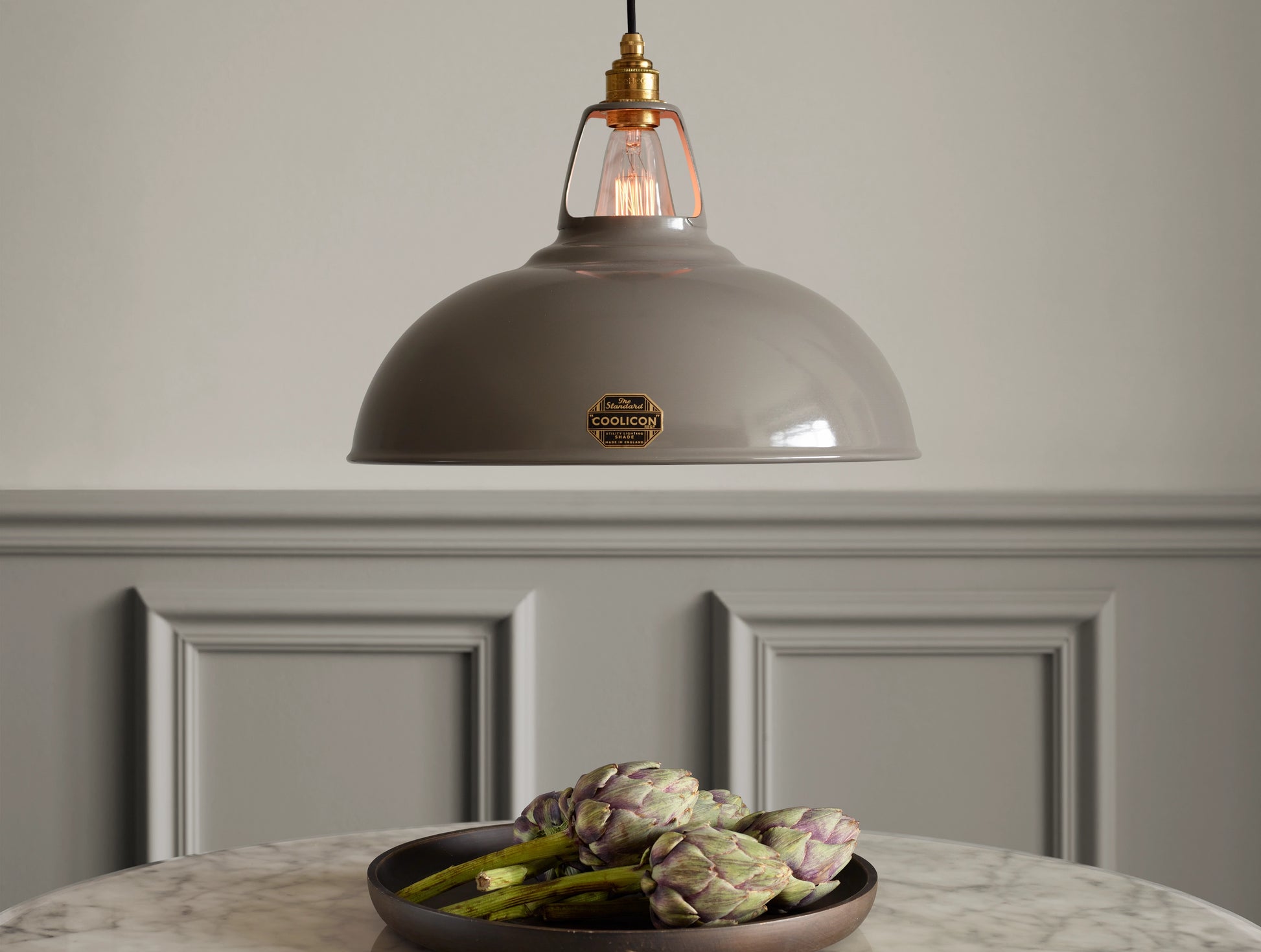 A Large Coolicon Original Grey lampshade hanging over a marble table. Below there is a grey tray with a few artichokes stems