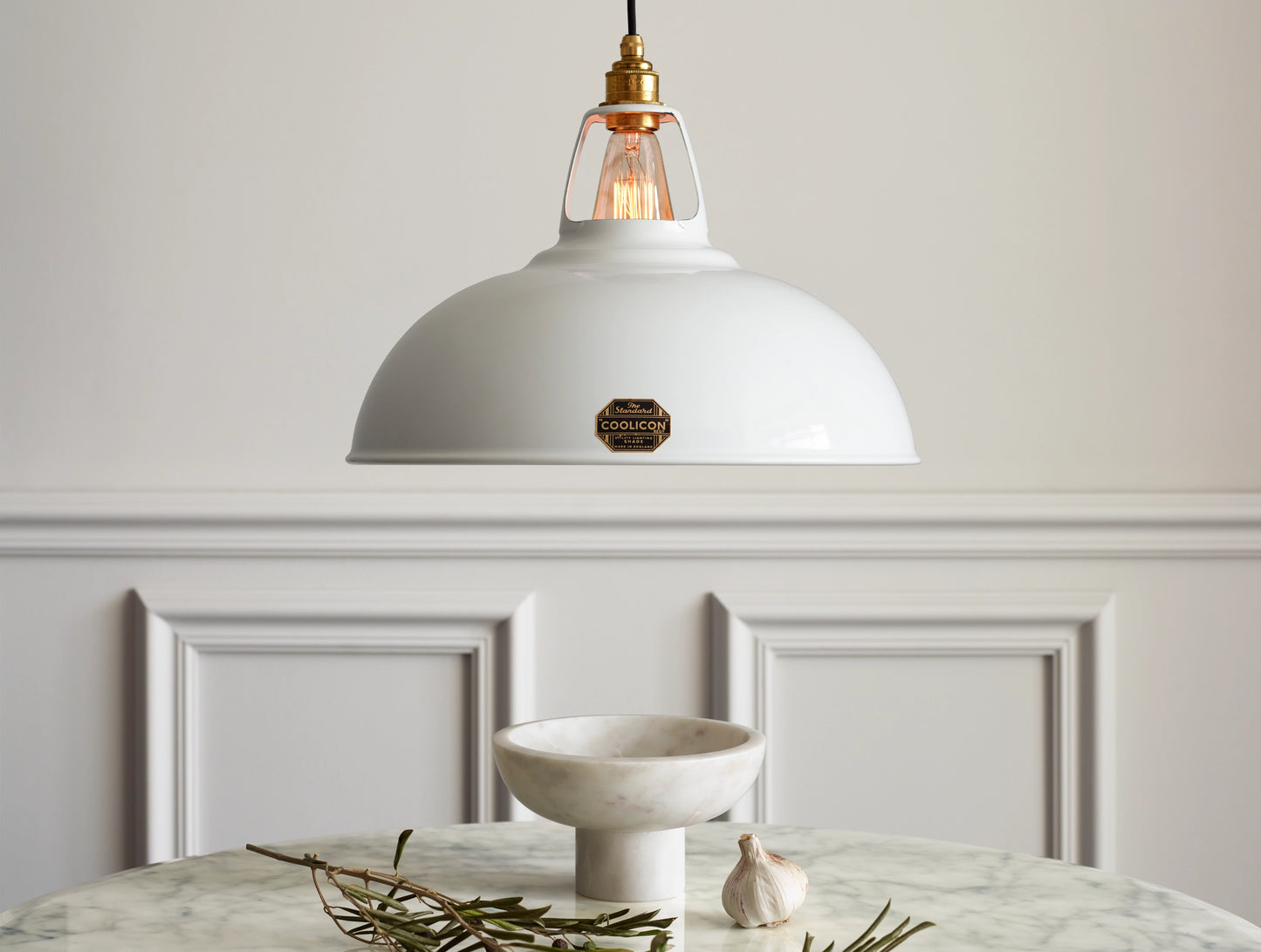 A Large Coolicon Original White lampshade hanging over a marble table. Below the shade is a marble salad bowl, a garlic bulb and a tree branch