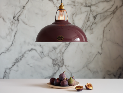 A Large Coolicon Metropolitan burgundy lampshade with a Signature Brass pendant set hanging above a table with tray of figs. One fig has been cut in half. The background is a marble wallpaper.