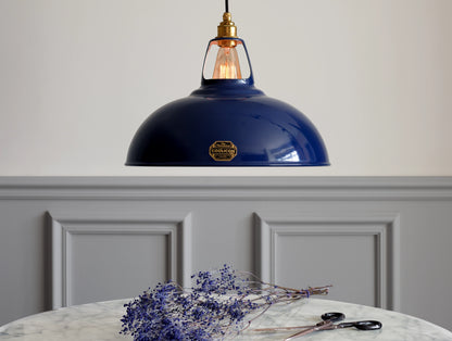 A large Royal Blue Coolicon shade hanging over a marble table. There is a branch of dried broom blue flowers underneath, along with a rusty pair of scissors